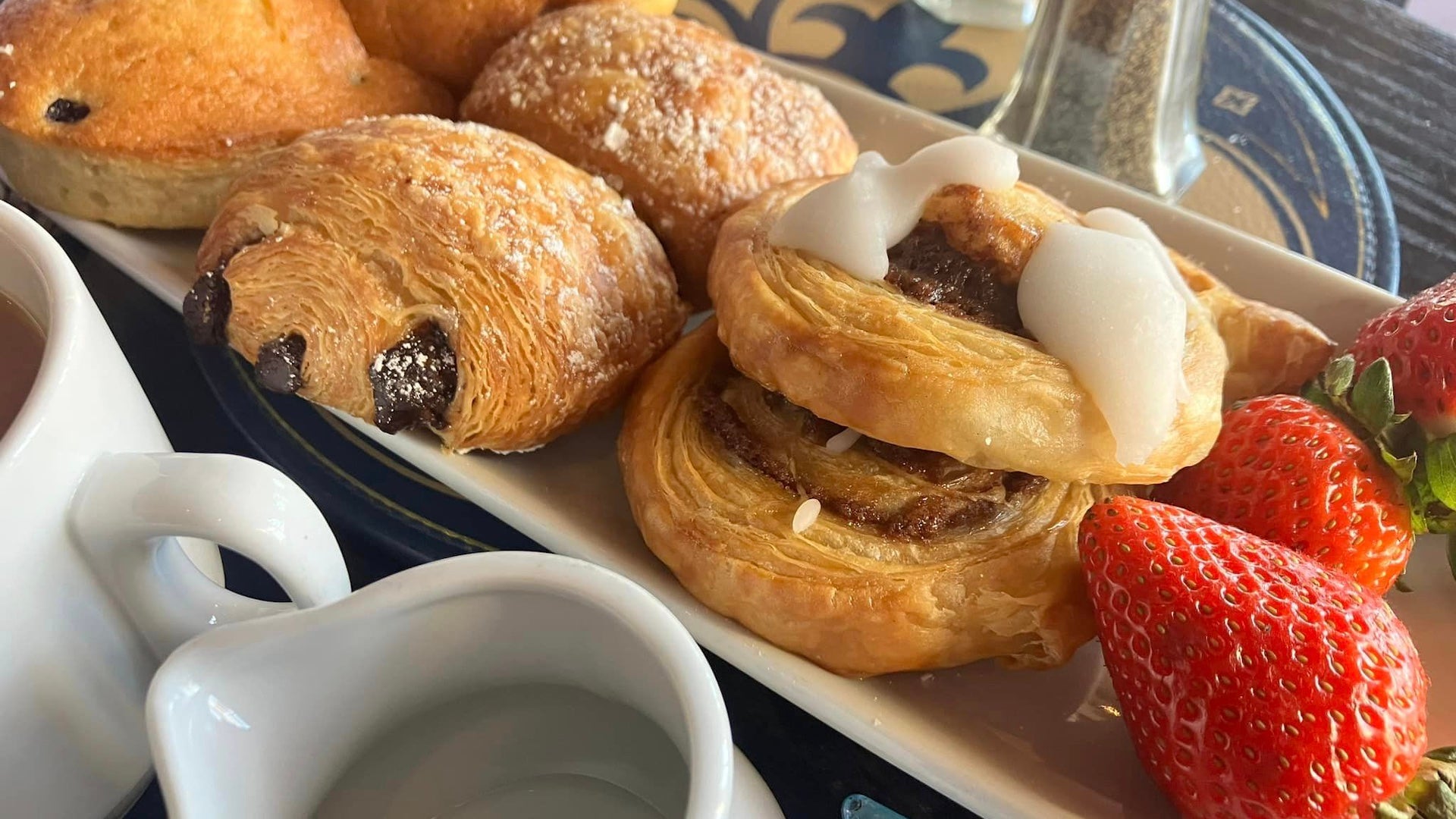 Pastries and fruit on a white plate next to a cup of coffee
